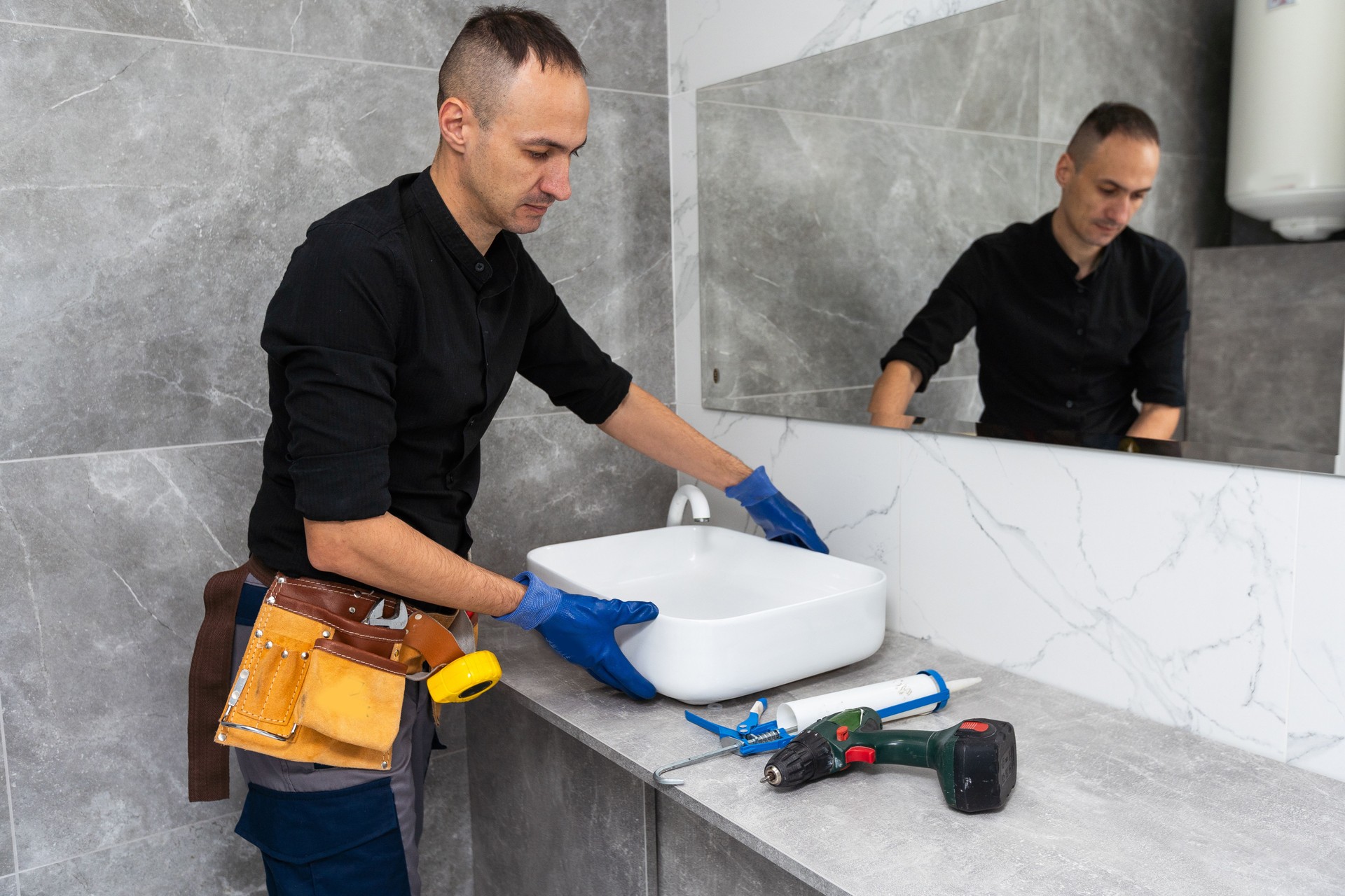 Professional plumber, male worker in uniform installing sink and water pipe in new apartment
